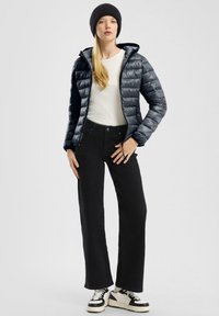 Padded navysblaue Jacke mit Kapuze und Reißverschluss, weißes Langarmshirt, schwarze weit geschnittene Jeans und schwarz-weiße Sneakers mit dicken Sohlen.