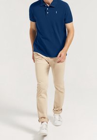 Námořnická polo košile s dvěma knoflíky, krátkým rukávem a malým vyšitým logem; béžové slim-fit kalhoty a bílé tenisky.