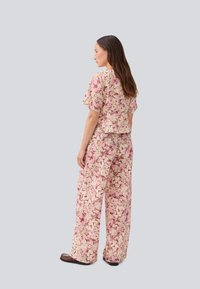 Completo a due pezzi realizzato in tessuto leggero con un motivo floreale in rosa e crema. Comprende una maglietta a maniche corte e pantaloni a gamba larga.
