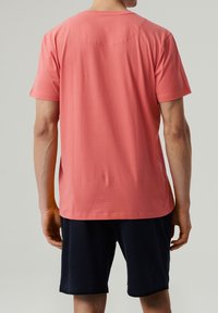 Koronowy bawełniany t-shirt z krótkim rękawem i okrągłym dekoltem, charakteryzujący się gładką teksturą i prostym wykończeniem, noszony z ciemnonawigacyjnymi szortami.