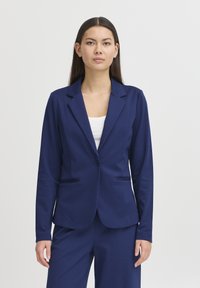 Blazer azul marino en tela suave, con cierre de un botón en la parte delantera, solapas con muesca y dos bolsillos frontales, combinado con pantalones a juego.