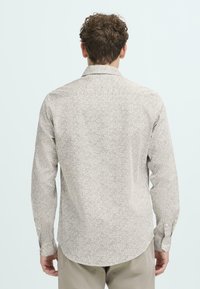 Lys beige langermet skjorte med et spredt mønster av svarte prikker, mykt stoff, krage med knapper og slim fit-silhuett.