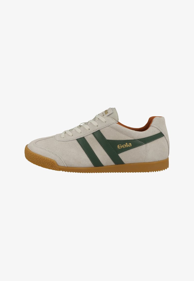 Zamszowe sneakersy z zielonymi paskami i złotym logo. Mają teksturowaną gumową podeszwę i wyściółkę wokół kostki, w kolorze białym i beżowym.