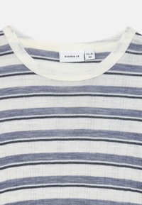Camisa de manga curta às riscas em creme claro e azul marinho, com riscas de largura variada e decote redondo; feita de um tecido macio e texturizado.
