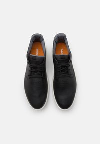 Baskets noires avec une tige texturée, semelle blanche et accents gris. Comprend des perforations et des lacets noirs. L'intérieur a une semelle intérieure orange.