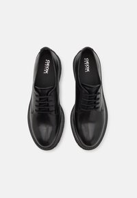 Chaussures en cuir noir avec une finition lisse, bout rond et système de laçage. Présentent un design minimaliste et un logo sur la semelle intérieure.