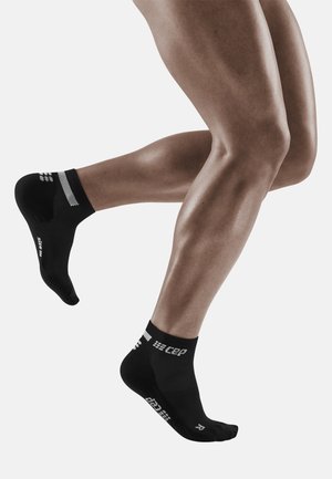 Black athletic socks with white accents, low-cut design, textured fabric, and printed logos on the sides, worn on a person's feet.