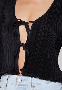 Haut noir plissé avec un décolleté en V profond et un détail noué à l'avant, doté d'un ourlet festonné. Porté avec un short en jean bleu clair taille haute.