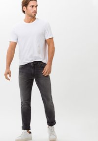 Fitted white short-sleeve T-shirt paired with dark gray jeans, featuring a classic cut, medium wash, and rolled cuffs. Worn with white sneakers.