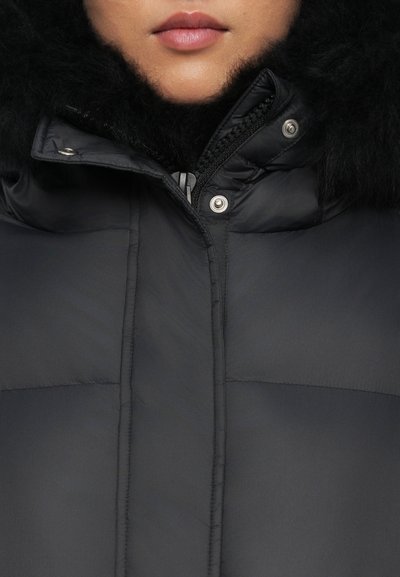 Black puffer jacket with a fur-lined hood, featuring a zipper closure and snap buttons, soft texture, and quilted pattern on the fabric.
