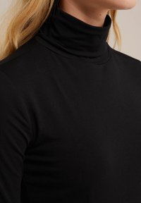 Černý rolák z měkké, elastické tkaniny. Úzký střih s vysokým límcem, hladká textura a minimální švy.