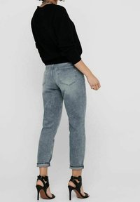 Maglione nero a maglia, jeans blu chiaro sbiaditi con risvolti, e sandali neri con tacco alto e design aperto sulla punta.