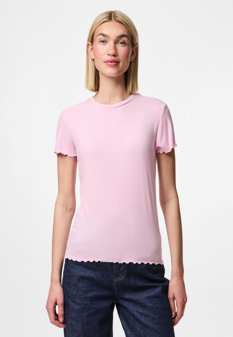 Camiseta corta de manga corta de color rosa con cuello redondo y dobladillo con forma de concha. La textura de la tela es suave. Se lleva con jeans de mezclilla oscura.
