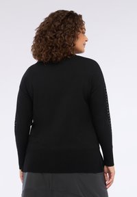 Maglione nero a maglia con orlo a coste e maniche lunghe, caratterizzato da borchie lungo il lato. Tessuto morbido, vestibilità rilassata e design di lunghezza media.