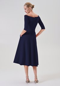Marineblaue, schulterfreie Kleid mit Dreiviertelärmeln und Taschen. Ein ausgestellter Rockdesign ergänzt eine glatte, weiche Textur.