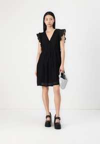 Vestido preto de renda com um decote profundo em V, mangas em babados e uma saia em camadas. Usado com sapatos de plataforma pretos e uma clutch prateada.