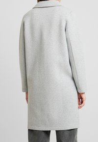 Grijze, middellange jas gemaakt van zacht materiaal. Heeft lange mouwen, een klassieke kraag en een rechte silhouet met minimale details.
