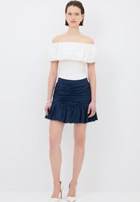 Top bianco off-shoulder con scollatura a volant, abbinato a una gonna blu navy con orlo a volant a strati e texture arricciata.