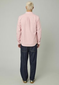 Chemise à rayures rouges et blanches à manches longues avec un col boutonné, associée à un jean bleu foncé et des baskets marron.