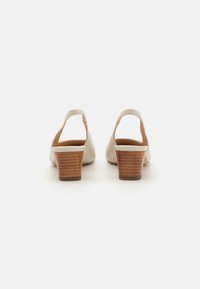 Beige lær slingback hæle med en træblokhæl og åben bagside, der har en glat tekstur og minimalistisk stil.