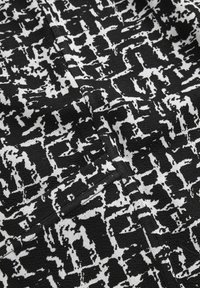 Schwarz-weißer strukturierter Stoff mit unregelmäßigen geometrischen Mustern und einem kleinen rechteckigen Taschendetail nahe der Mitte.