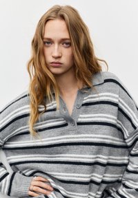 Grijs-wit gestreepte pullover met een kraag met knopen en lange mouwen. Zachte textuur en een relaxed model.