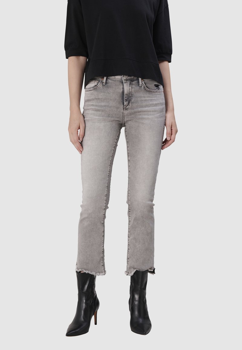 Jean en denim gris avec une légère effilochure à l'ourlet, taille haute et délavage subtil. Assorti à des bottines à talons noires.