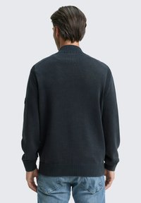 Maglione grigio scuro a maglia con colletto, polsini e orlo a costine, caratterizzato da una finitura testurizzata e una vestibilità rilassata, abbinato a jeans azzurri chiari.