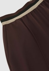 Pantaloni burgundy confecționați dintr-un material moale, cu talie elastică având dungi negre și bej, și un design plisat pentru un plus de textură.