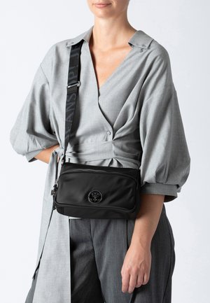 Borsa a tracolla nera in nylon con texture liscia, chiusura con zip e dettaglio del logo circolare sul davanti. Tracolla regolabile.