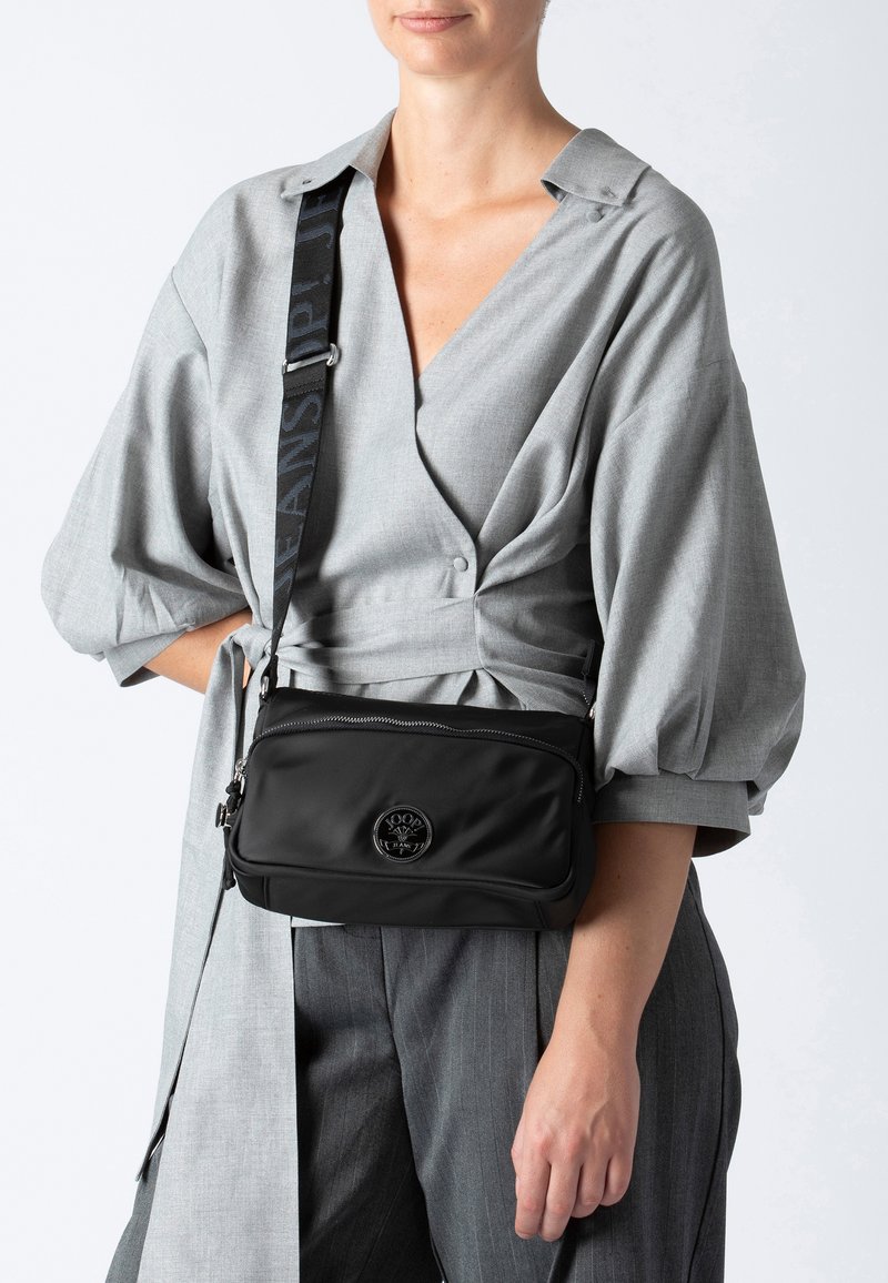 Borsa a tracolla nera in nylon con texture liscia, chiusura con zip e dettaglio del logo circolare sul davanti. Tracolla regolabile.