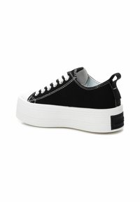 Zapatilla de lona negra con suela de plataforma de goma blanca, costuras blancas y tira trasera. Presenta un diseño clásico con cordones y cuello acolchado.