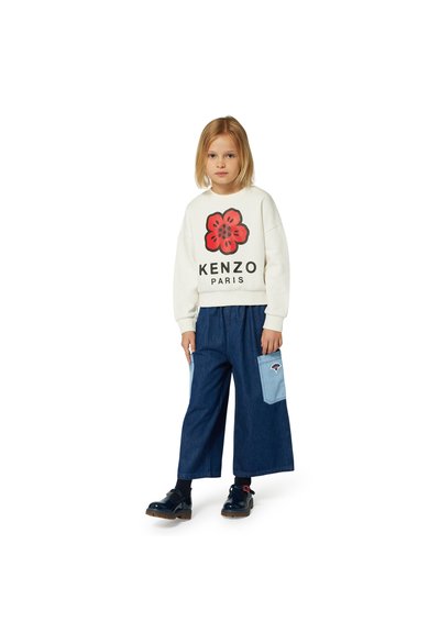Sweat-shirt blanc avec un imprimé fleur rouge et le texte "KENZO PARIS", associé à un pantalon large en denim foncé avec une poche bleu clair.