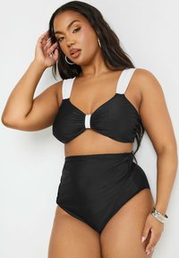 Svart tvådelad baddräkt med en knuten, vadderad bh-topp och höga byxor; har vita axelremmar och sidofållningsdetalj.