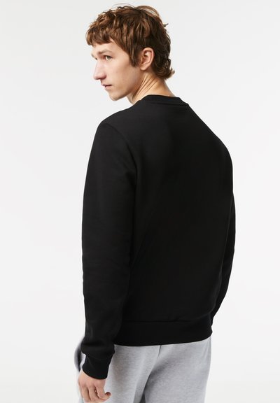 Sweatshirt noir avec un col rond, poignets et ourlet côtelés, associé à des joggings gris. Texture lisse, design ajusté, couleur unie.