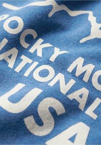Tela de algodón azul con el texto blanco "ROCKY MOUNTAIN" y "NATIONAL PARK USA", con un acabado suave y texturizado.