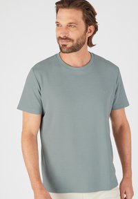 Camiseta de manga corta azul claro con cuello redondo, tejido texturizado y un sutil logo en el pecho. Corte regular, diseño casual.