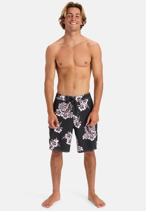 Schwarze Badeshorts mit weißem Hibiskus-Blumenmuster, ausgestattet mit einem Kordelzugbund und Seitentaschen, aus leichtem Stoff gefertigt.