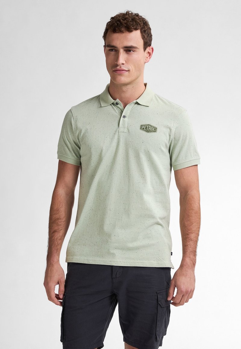 Polo shirt verde chiaro con texture maculata, maniche corte, pattina con due bottoni e un piccolo logo "PETROL" sul lato sinistro del petto.