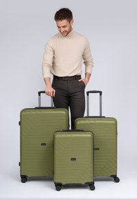 Set van drie olijfgroene harde koffers met een gemêleerd zigzagpatroon, zwarte accenten, dubbele wielen en uitschuifbare handvatten.