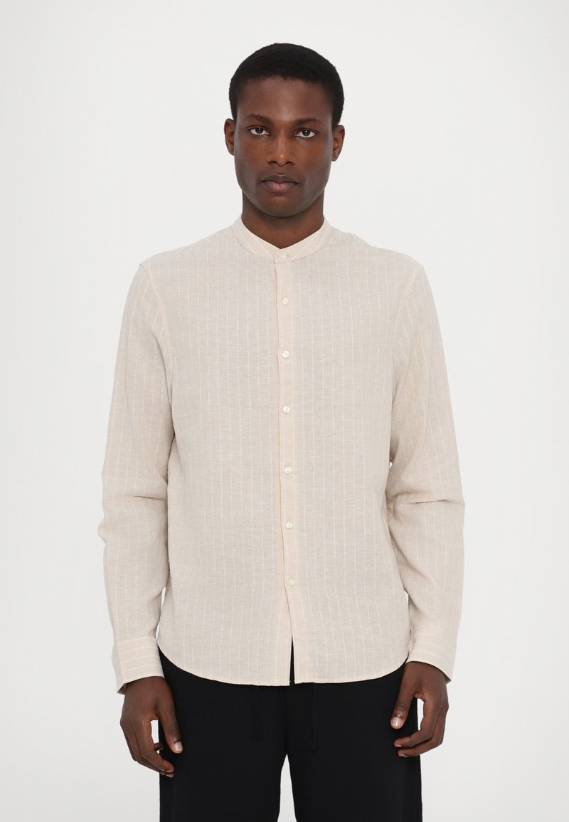 Camicia a maniche lunghe beige chiaro con colletto alla cinese, caratterizzata da sottili righe verticali, chiusura frontale con bottoni e un tessuto morbido e testurizzato.