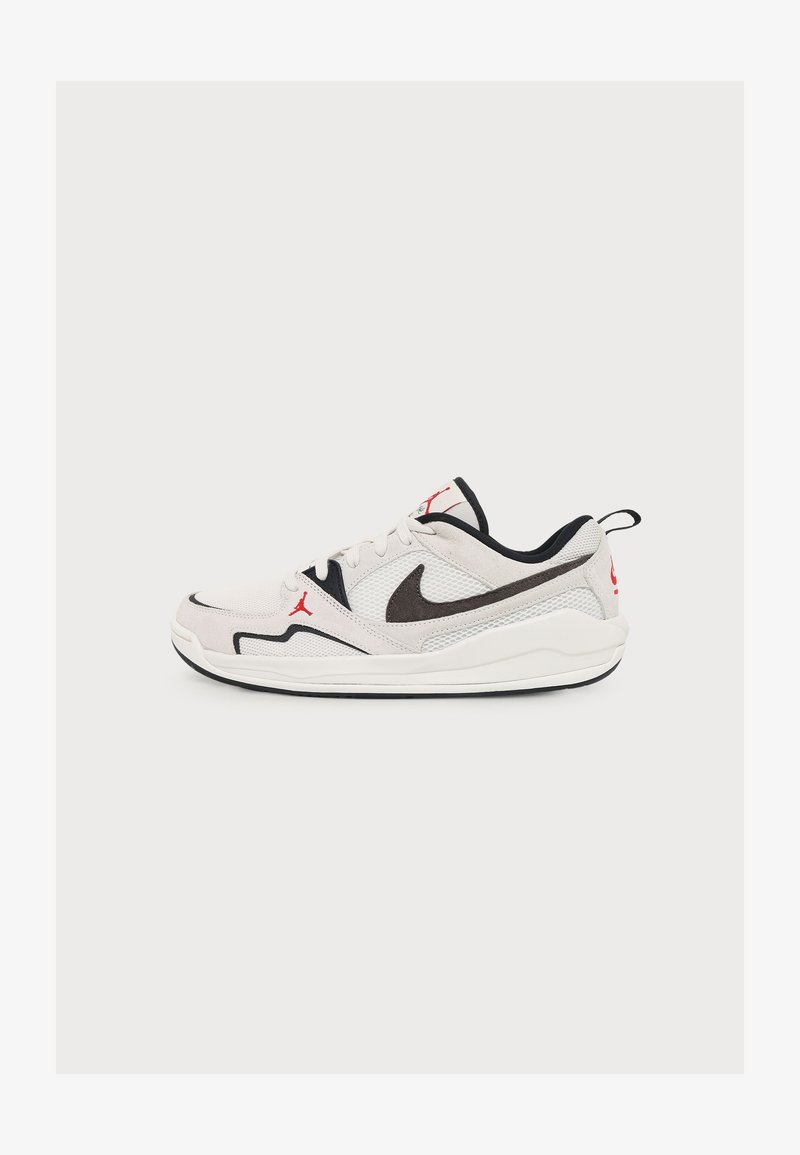 Άσπρο και μαύρο χαμηλό sneaker Nike Air Jordan με κόκκινα λογότυπα και ύφασμα από δίχτυ σε απλό ανοιχτό φόντο.
