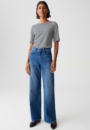 Striped, short-sleeved t-shirt in black and white paired with wide-leg blue jeans. Jeans feature pockets and a buttoned waist. Black shoes.