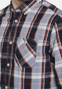 Chemise à boutons à carreaux présentant des couleurs bleu marine, gris et orange. Fabriquée en coton, elle comporte une poche poitrine et des détails de couture contrastés.