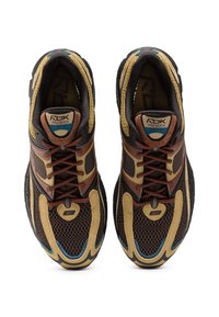 Brūnu, bēšā un melnu Reebok Premier sporta apavu pāris ar sietiņveida paneļiem, sasienamiem aizdariem un mīkstām apkaklēm, skatīts no augšas.