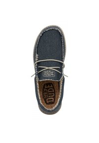 Baskets en toile bleu marine avec une texture tissée, des coutures beiges contrastées et une semelle intérieure en liège arborant le logo noir "Hey Dude".