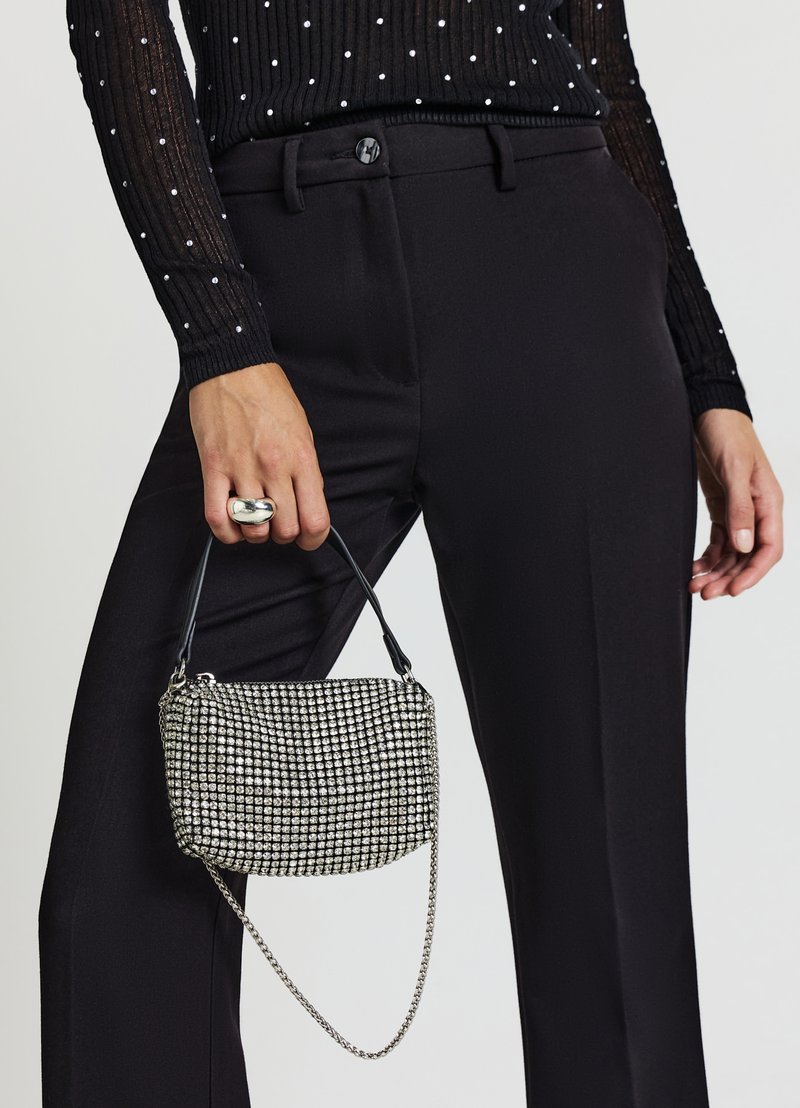 Maglietta nera a maniche lunghe con trama e pois bianchi; pantaloni neri a gamba larga; borsa argentata con borchie, tracolla e manico.