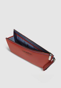 Pochette en cuir rouge à la texture lisse, fermeture zippée et intérieur bleu marine. Comprend des compartiments intérieurs et une sangle poignet amovible.