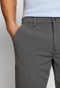 Gray tailored trousers made of a smooth, textured fabric. Features a narrow waistband and a single button closure.