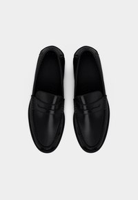 Μαύρα δερμάτινα μοκασίνια με λεία επιφάνεια, υφασμένη ραφή γύρω από τις άκρες και διακοσμητική μπροστινή λωρίδα.